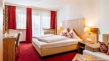 Habitación de hotel con una cama grande, un escritorio de madera, una silla, una mesita con un cuenco de fruta y un sofá.