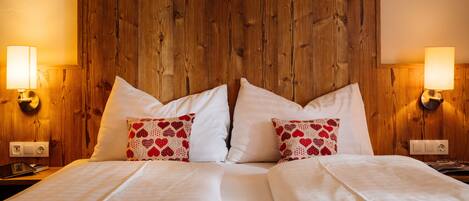 A double bed with white linens and heart-patterned pillows, wooden headboard, and wall-mounted lamps.