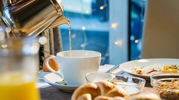 A breakfast setting with a cup being filled with a beverage, a plate of food, and a glass of orange juice.