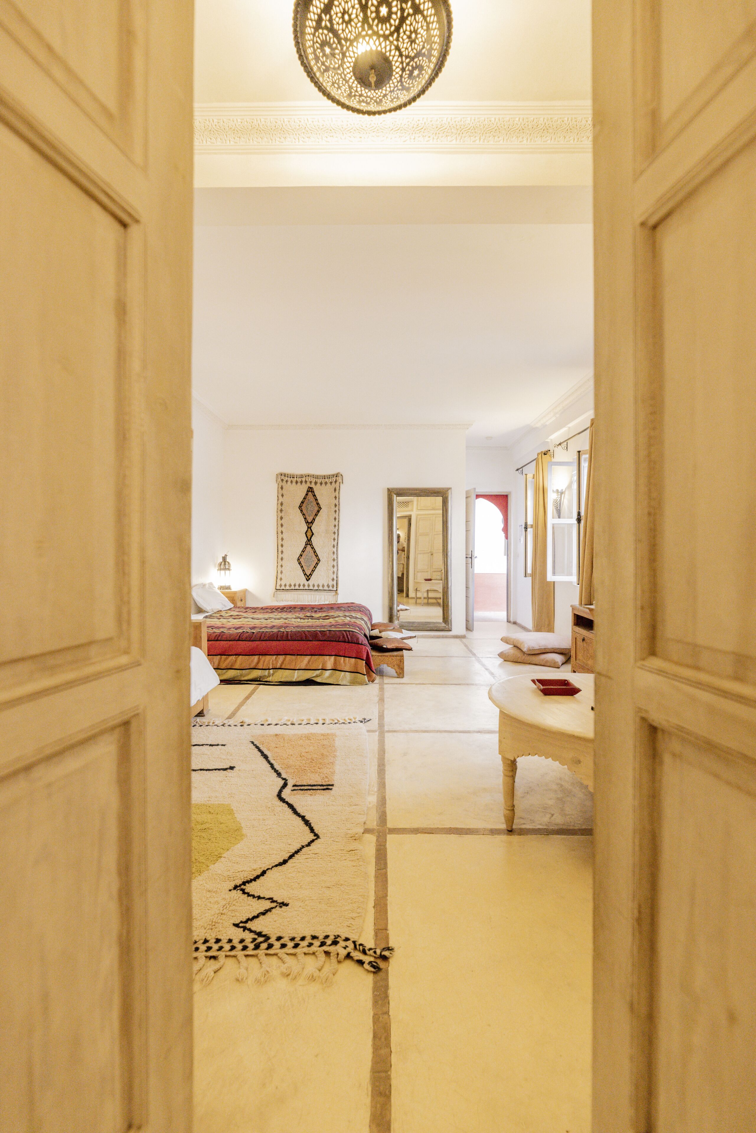 Una habitación con cama, espejo, alfombra y puerta que da a otra estancia.