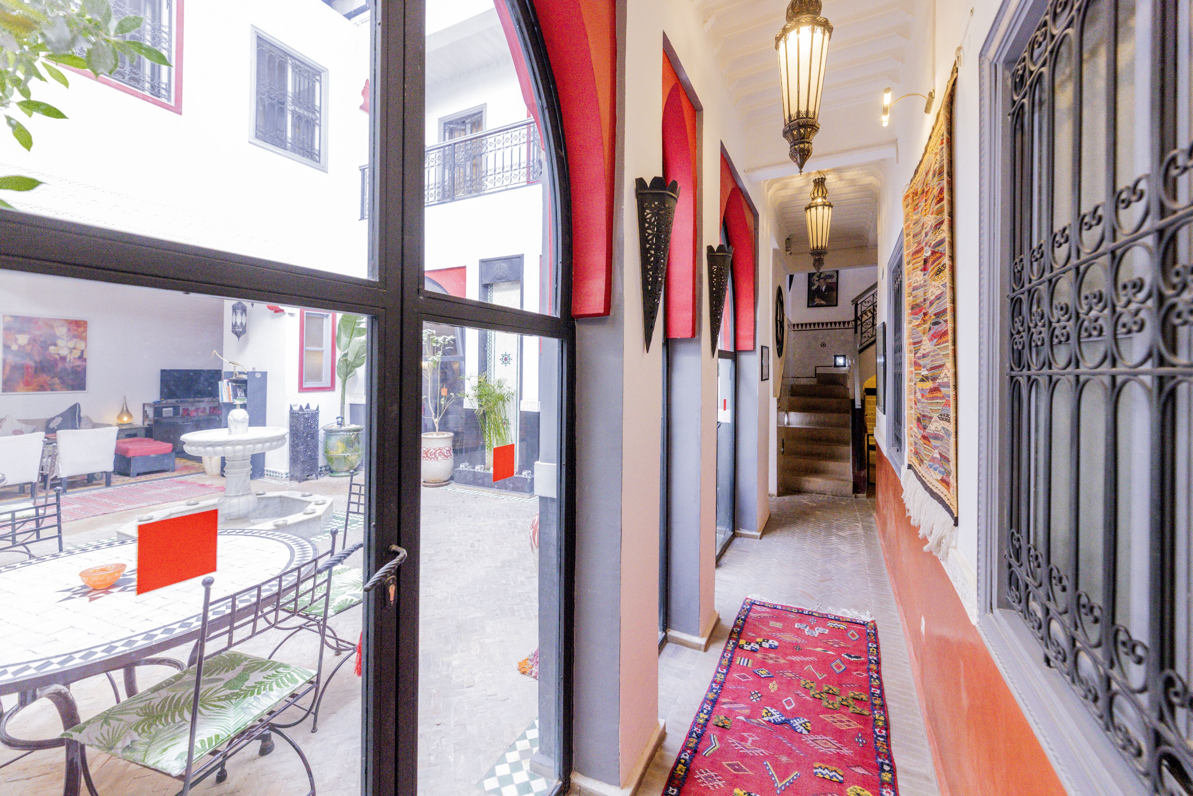 Un couloir d’hôtel avec un sol à carreaux, une moquette rouge et une vue sur l’espace extérieur aménagé pour les clients.