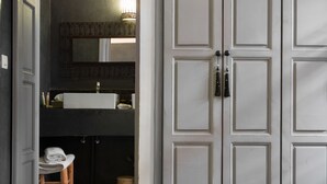 Une salle de bain avec un lavabo blanc, un miroir au-dessus et un tabouret en bois sur lequel sont posées des serviettes.