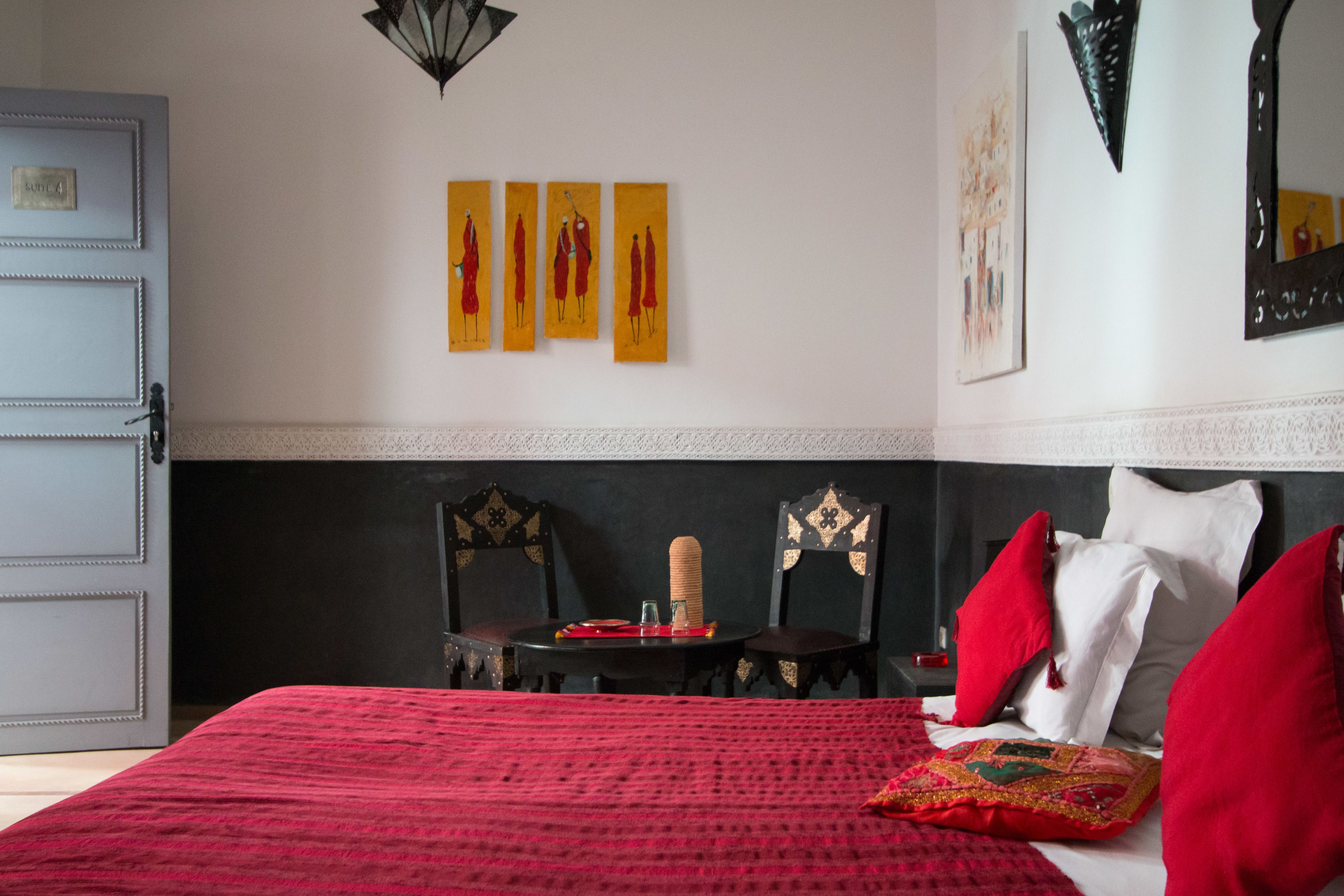 A hotel room with a large bed, red bedding, a small table with a candle, and artwork on the wall.