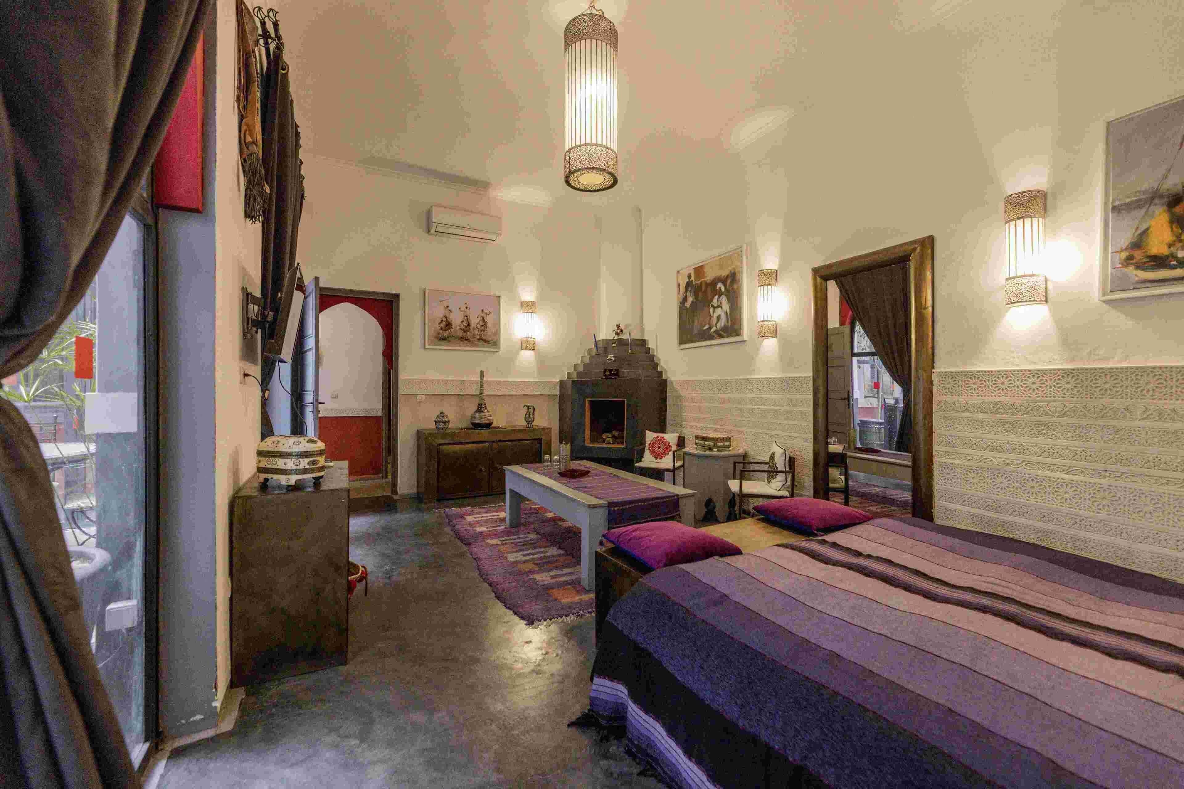 A room with a bed, a small table, a mirror, and a fireplace.