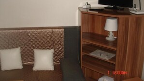 A hotel room with a wooden headboard, a flat-screen TV, a desk with a lamp, and a small white suitcase. - Pension Easy Journey (Prague)