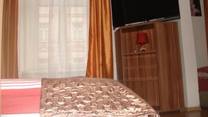 A hotel room with a bed, a TV mounted on the wall, and a wooden wardrobe. - Pension Easy Journey (Prague)
