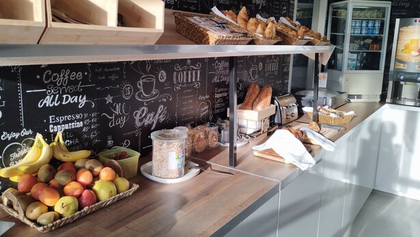 Mostrador de café con menú en pizarra, pan, bollería y exposición de frutas.
