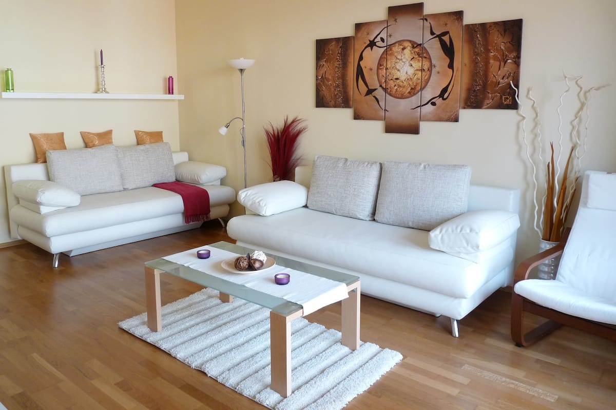A modern living room with a white sofa, a glass coffee table, and a large abstract painting on the wall.