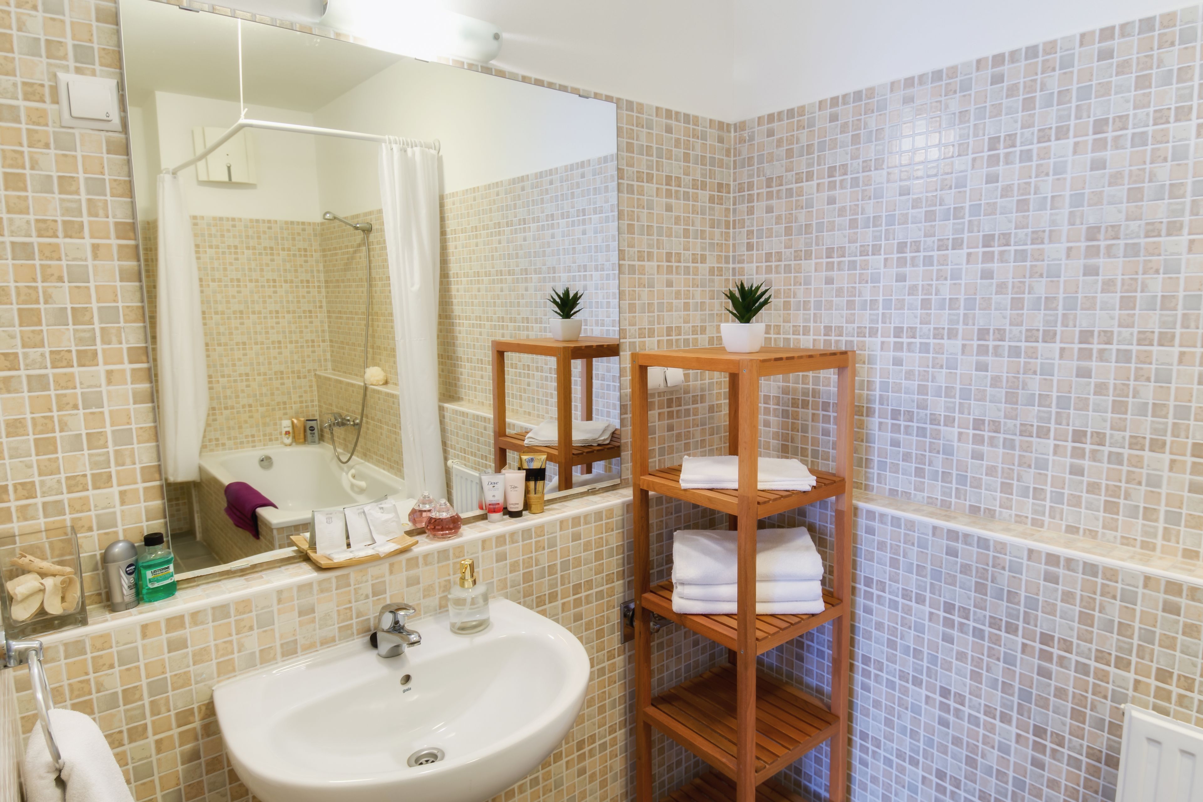 A bathroom with a sink, mirror, shower, and wooden shelves with towels.