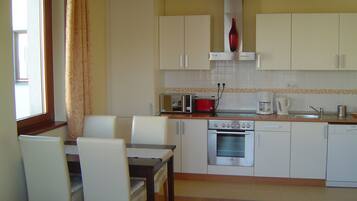 A compact kitchen with white cabinets, a dining table with chairs, a red toaster, a coffee maker, and a dishwasher.