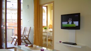 Una sala moderna con una mesa de centro de vidrio, un sofá blanco, un televisor de pantalla plana montado en la pared y una mesa de comedor de madera con sillas.