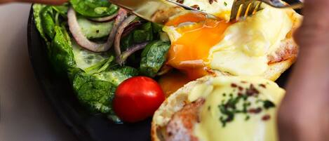 A person cutting an egg benedict on a plate with a side salad.