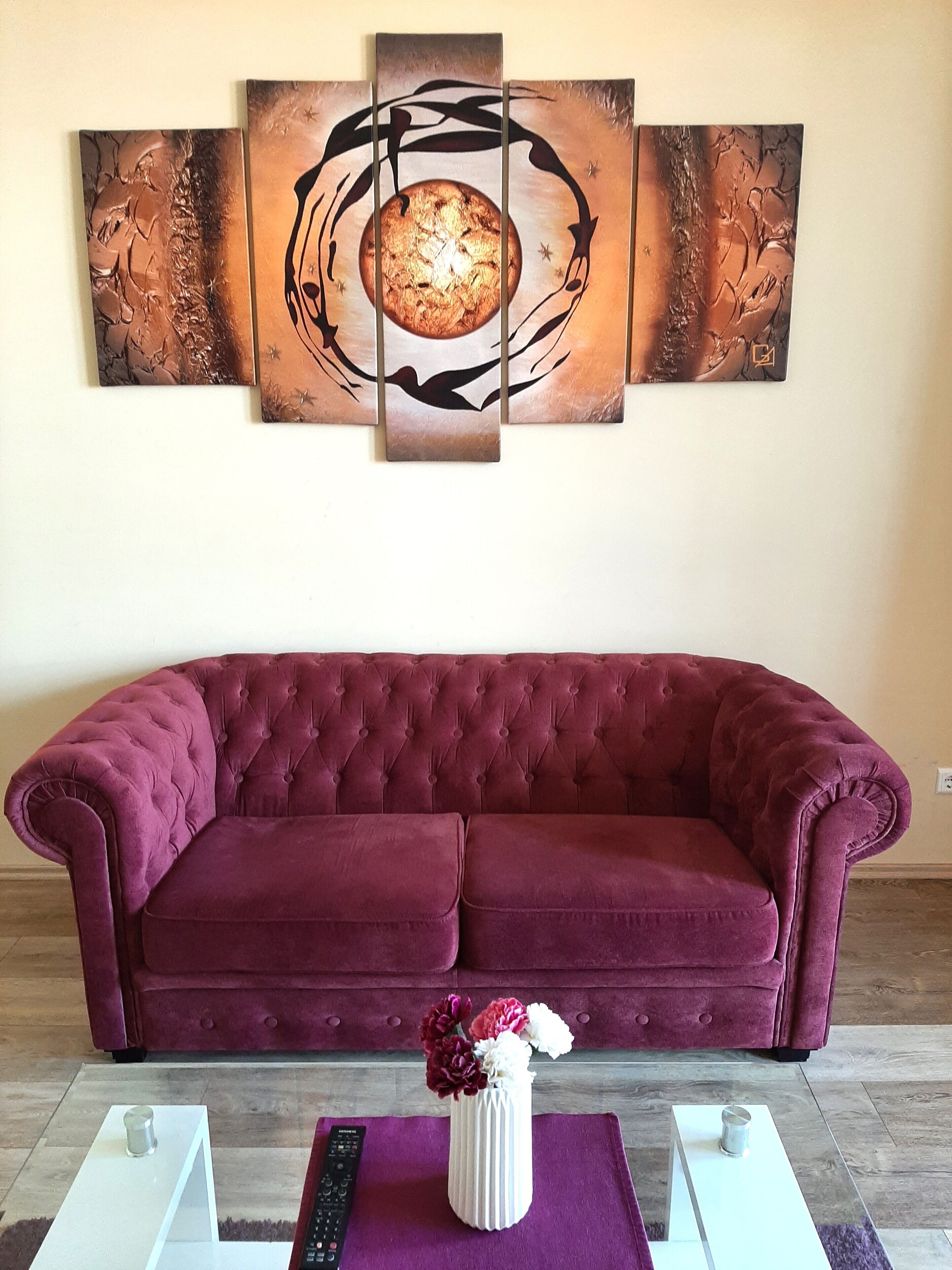 Un salon avec un canapé violet, un vase blanc rempli de fleurs et un grand tableau abstrait accroché au mur.