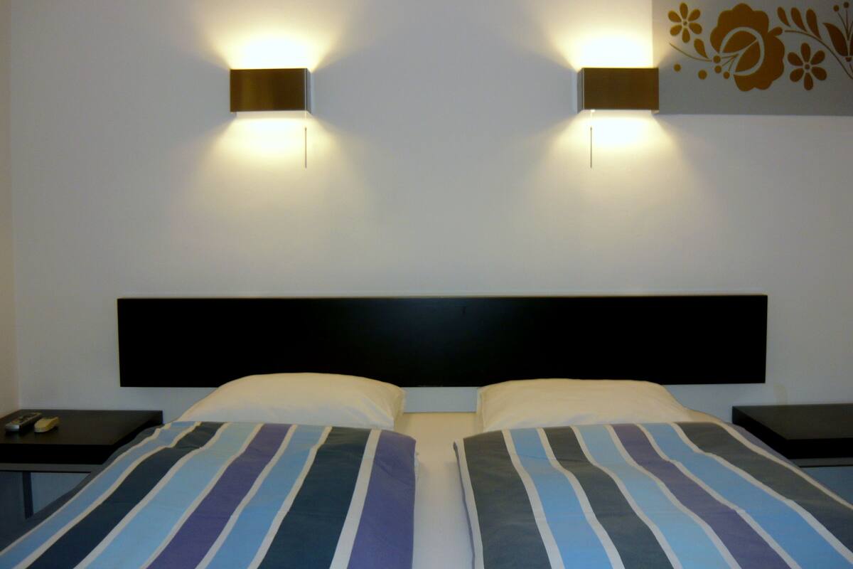 A hotel room with two beds, each with striped bedding, a black headboard, and two bedside tables with lamps.