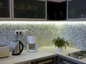 Une cuisine avec un mur recouvert de carreaux, une machine à café, un grille-pain et une plante.