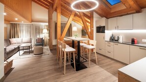 A modern kitchen with wooden beams, a dining area with a round table, and a cozy living room with a sofa and a lamp. - Grindelwalderhof (Grindelwald)
