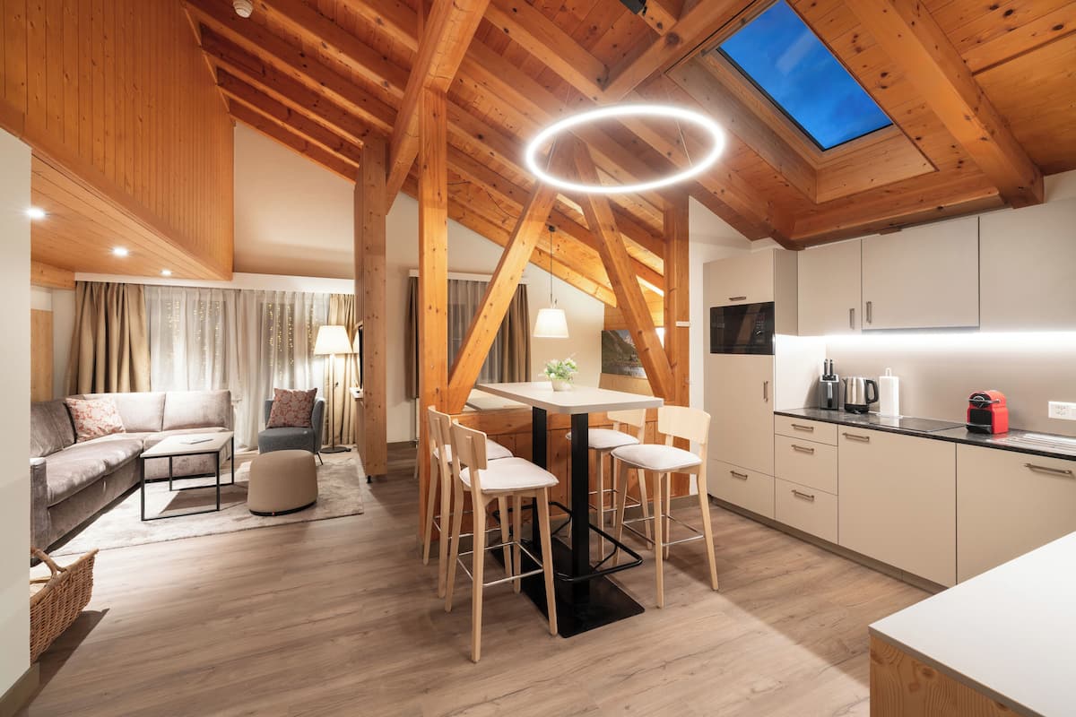 Uma cozinha moderna com vigas de madeira, uma área de refeições com mesa redonda e uma sala de estar aconchegante com sofá e abajur.