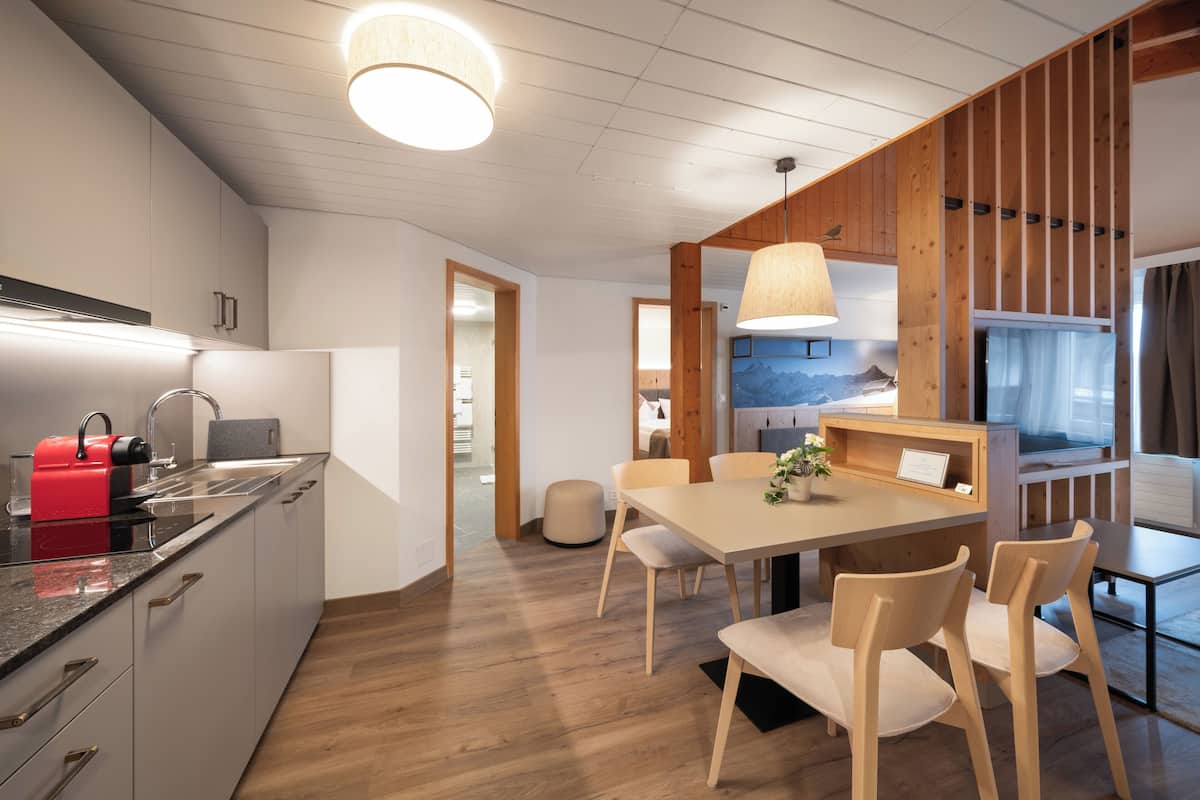Cozinha moderna com detalhes em madeira, área de jantar com mesa e cadeiras de madeira, e vista para as montanhas pela janela.