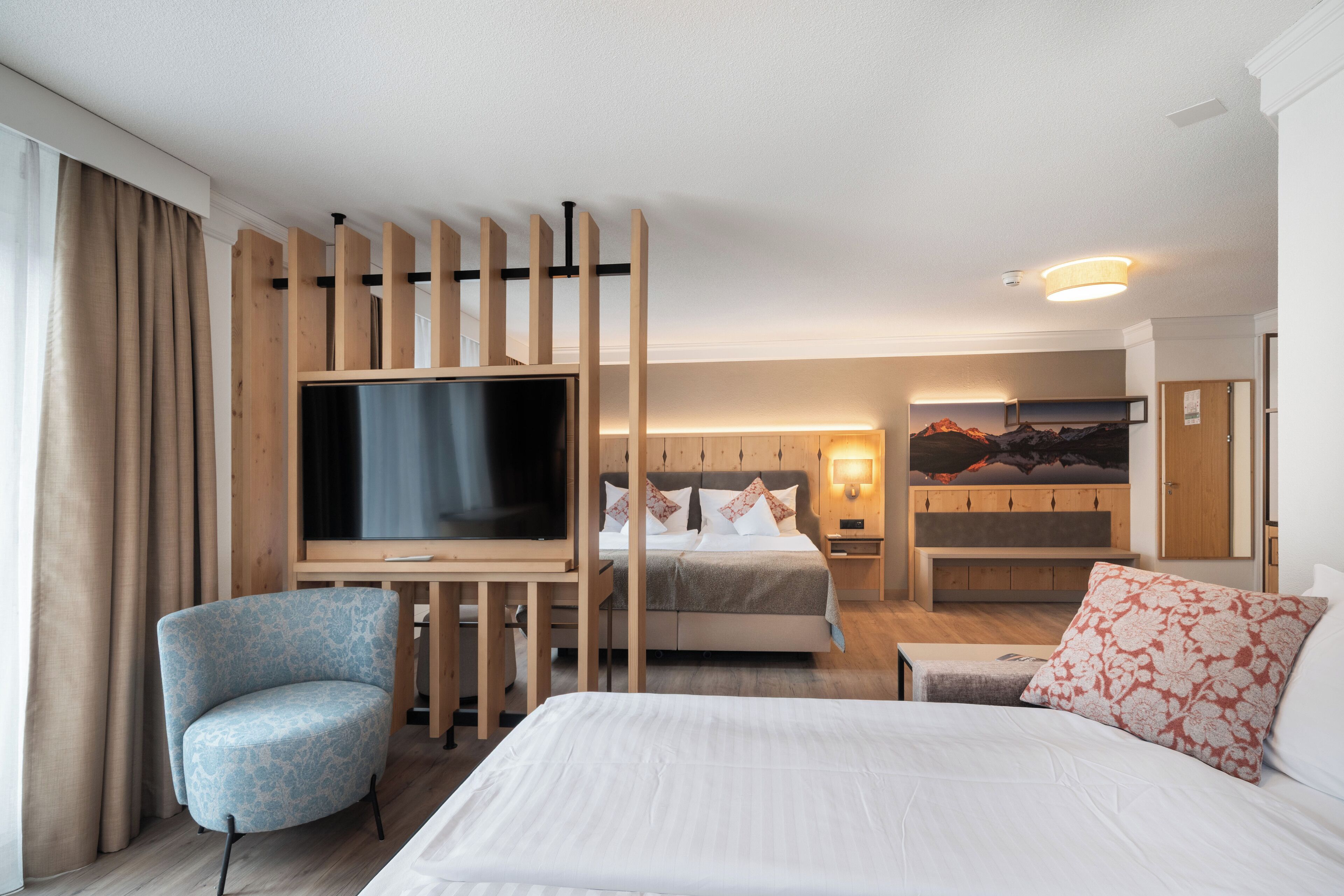 A hotel room with a bed, a TV, a chair, a desk, and a painting on the wall.