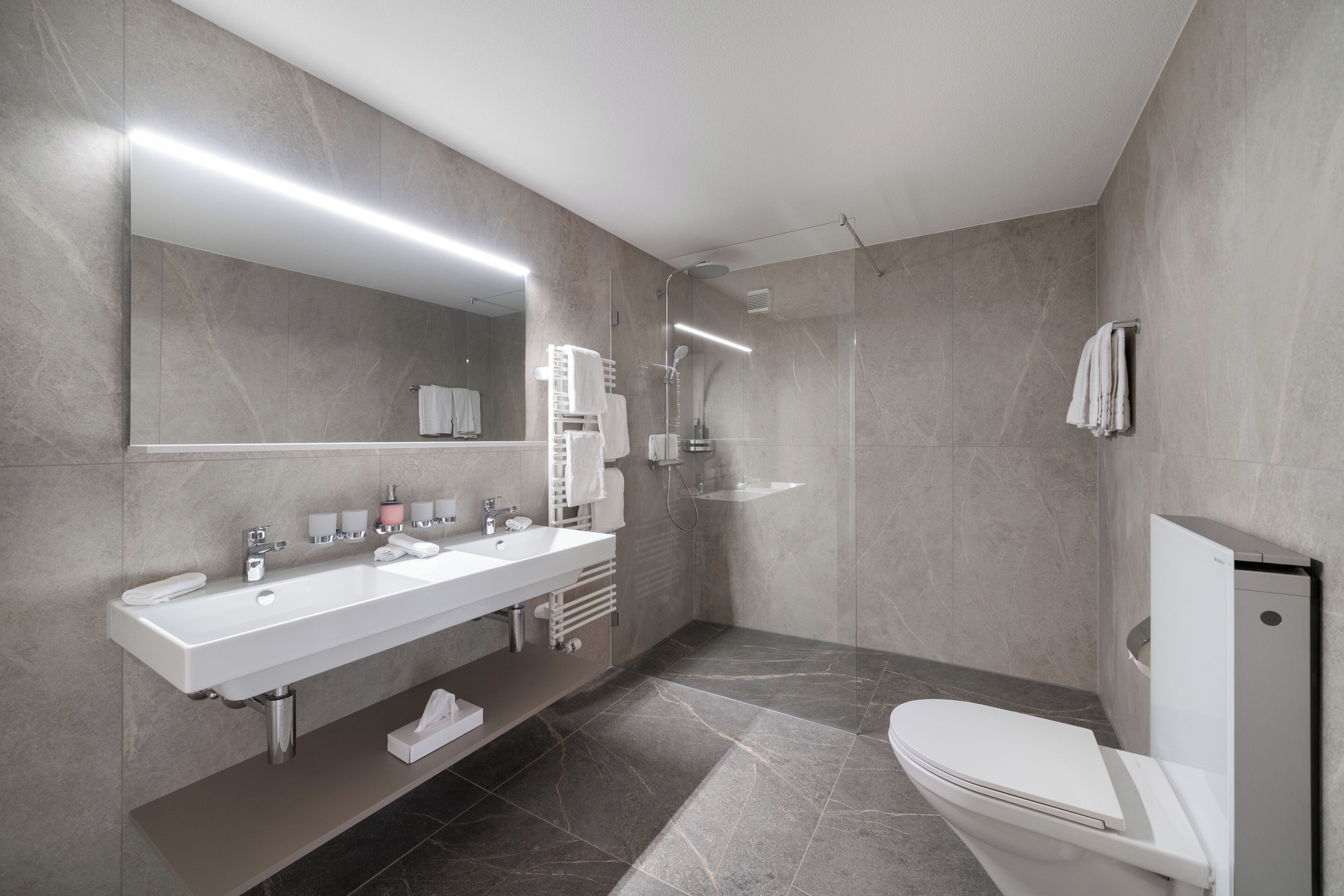 A modern bathroom with a large mirror, a white sink, a toilet, and a shower area.