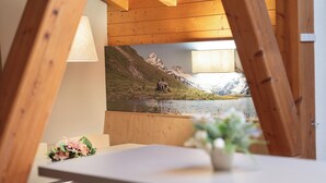 A room with a wooden ceiling, a table with a vase of flowers, and a wall-mounted painting of a mountain landscape. - Grindelwalderhof (Grindelwald)