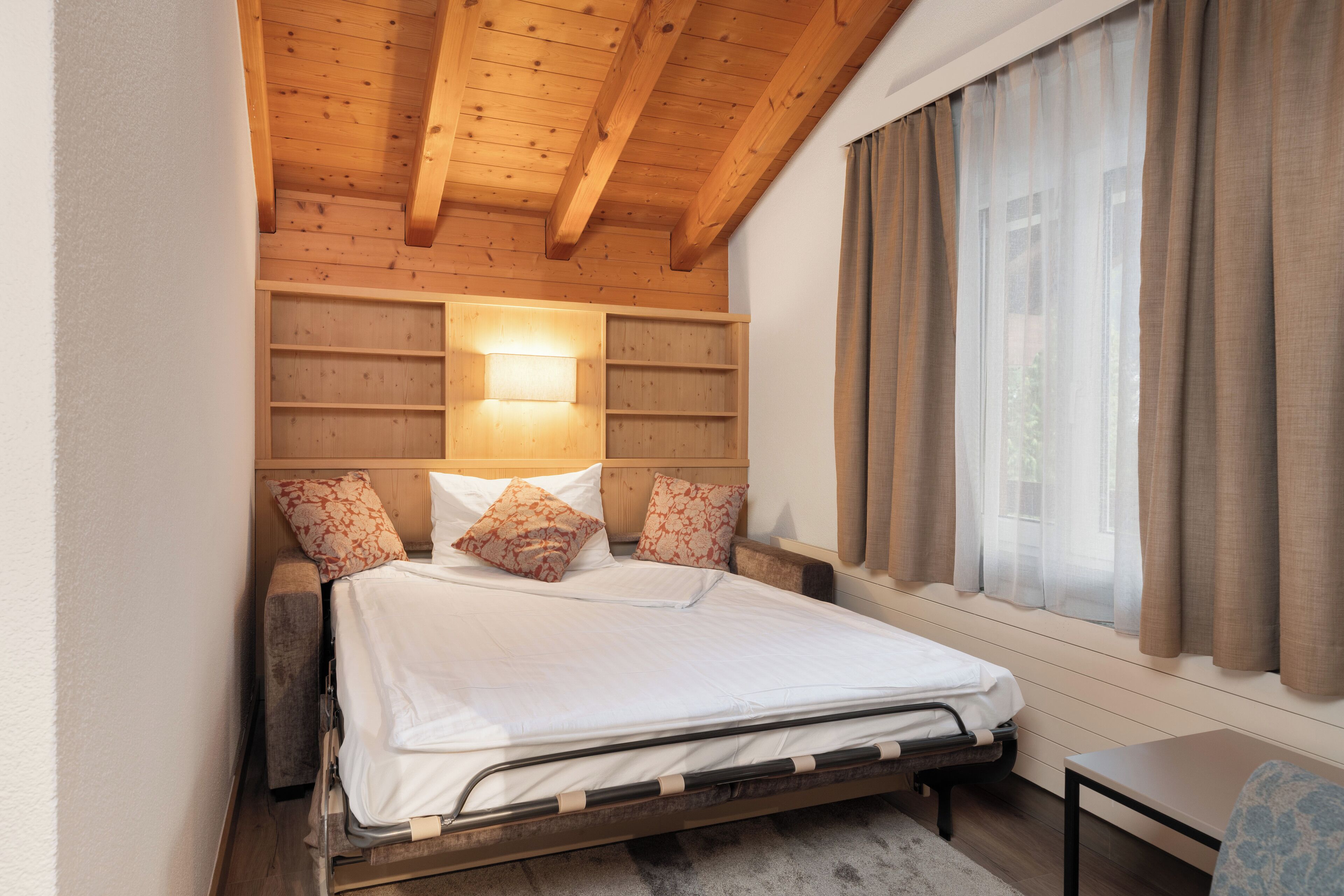 A bedroom with a wooden ceiling, a bed with white bedding, a nightstand, and a window with curtains.
