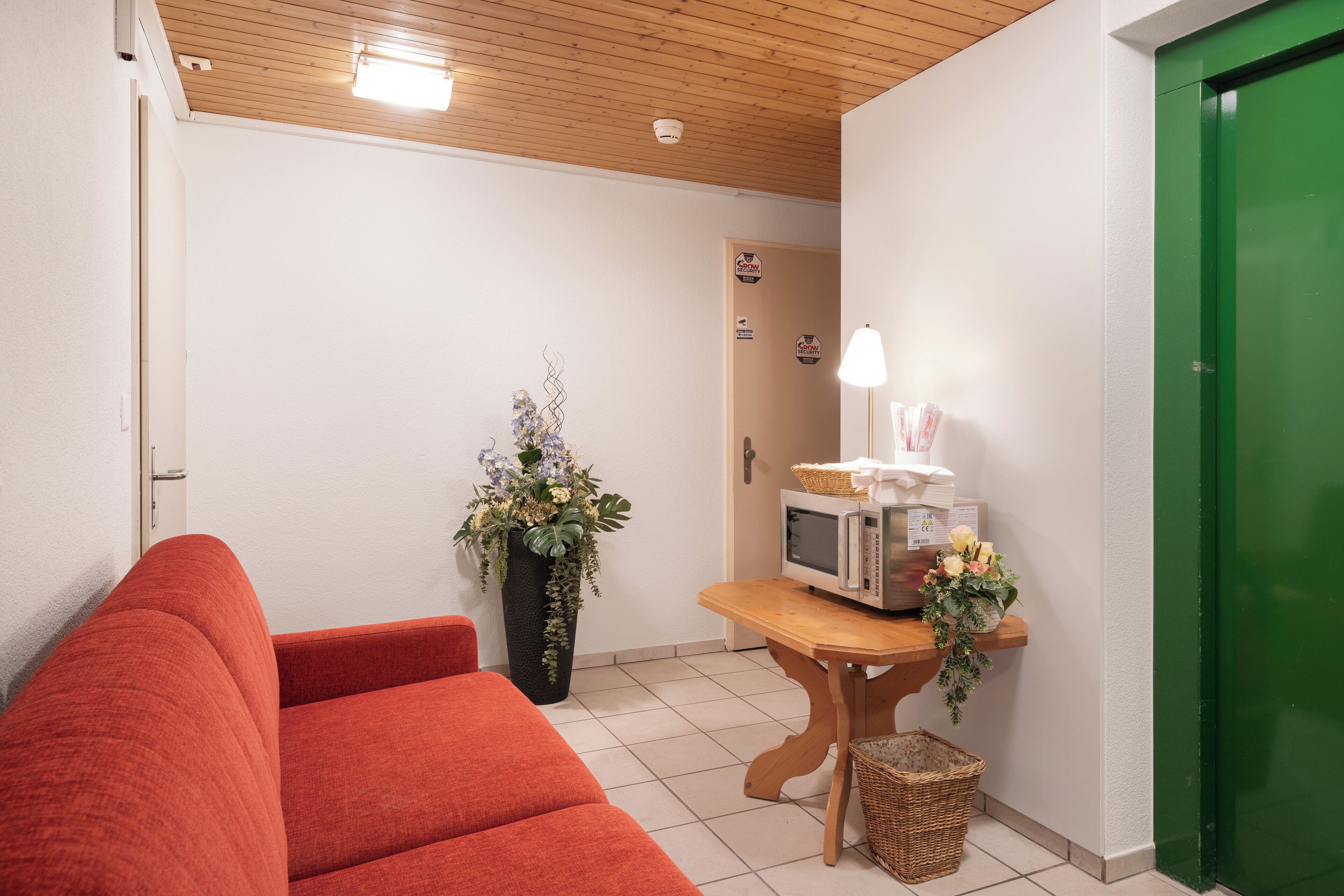 A room with a red sofa, a wooden table with a microwave, a basket, and a potted plant.
