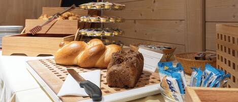 Un bufé de desayuno con pan, pasteles y aperitivos envasados sobre una mesa de madera.
