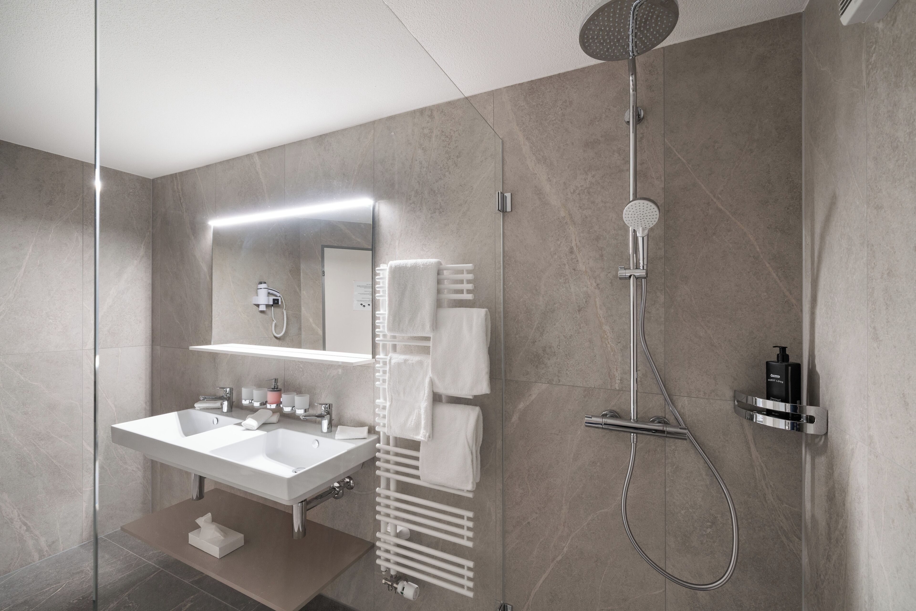 Un baño moderno con ducha de vidrio, tocador doble y perchero para toallas.