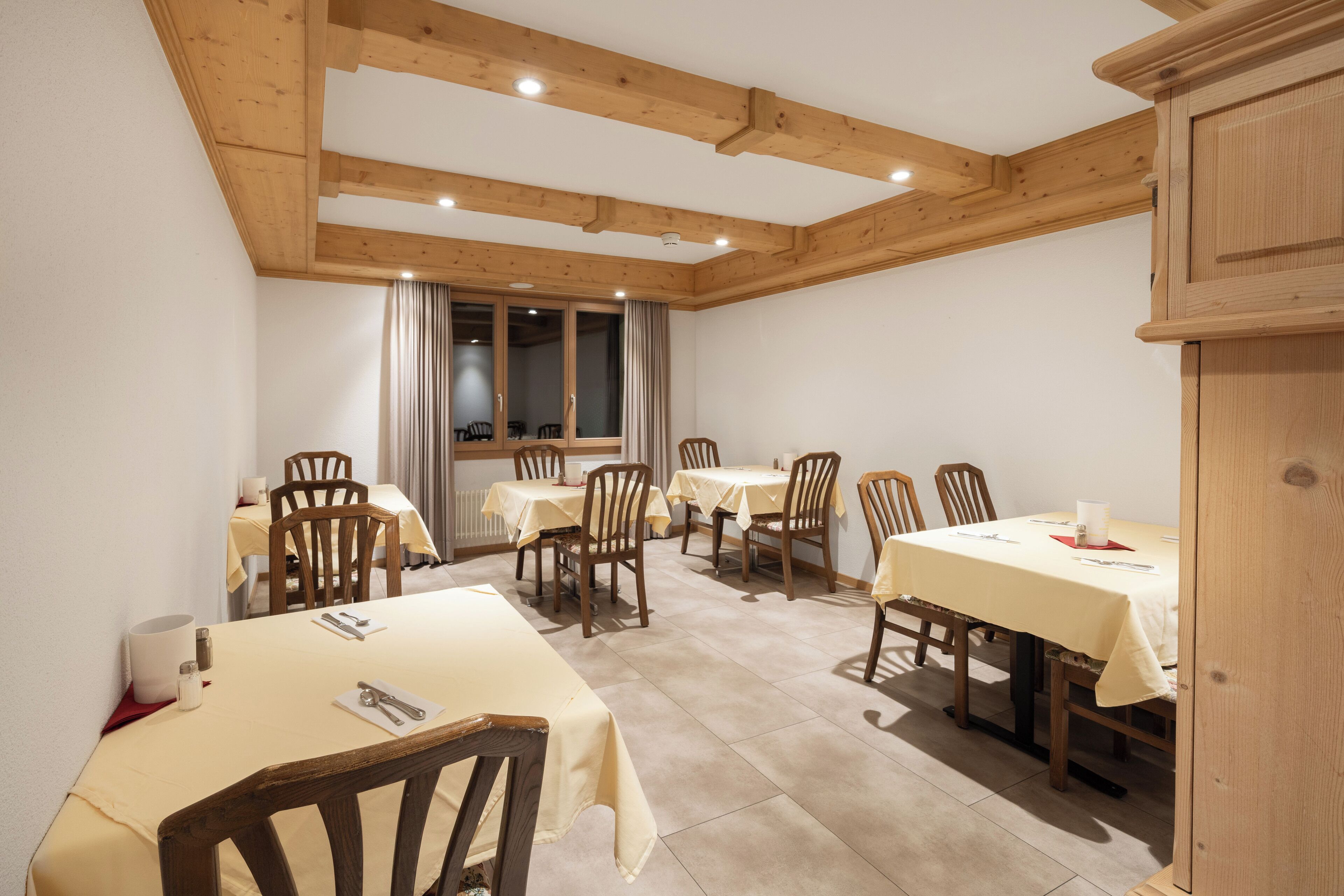 A dining area with wooden beams, multiple tables with yellow tablecloths, and wooden chairs.