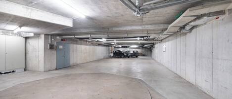 Un estacionamiento con paredes de concreto, suelo plano e iluminación en el techo.