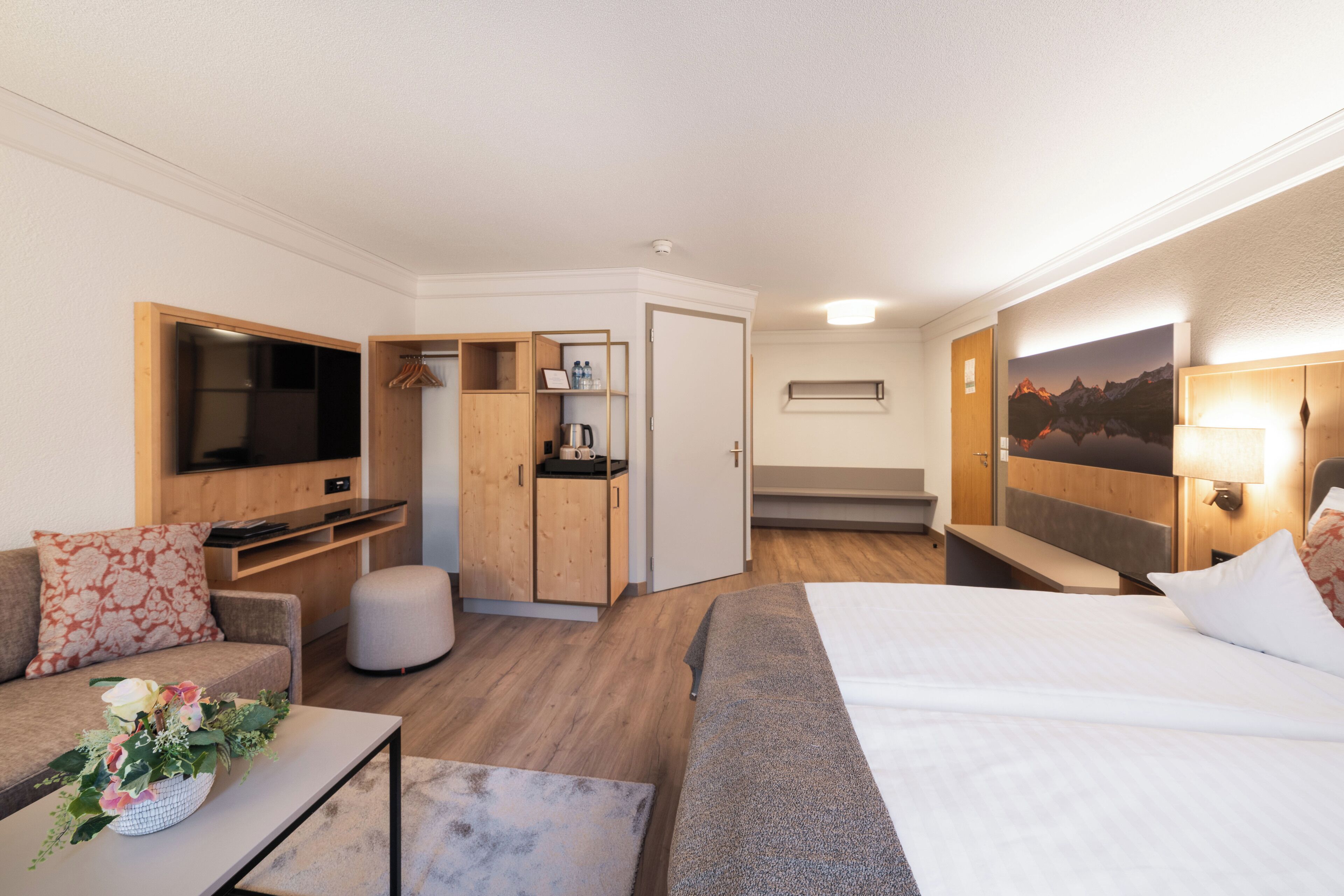 Una habitación de hotel moderna con cama, sofá, escritorio, televisor y un cuadro en la pared.