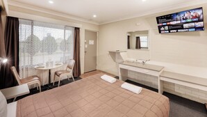 A hotel room with a bed, a desk, a chair, a TV, and a window with curtains.