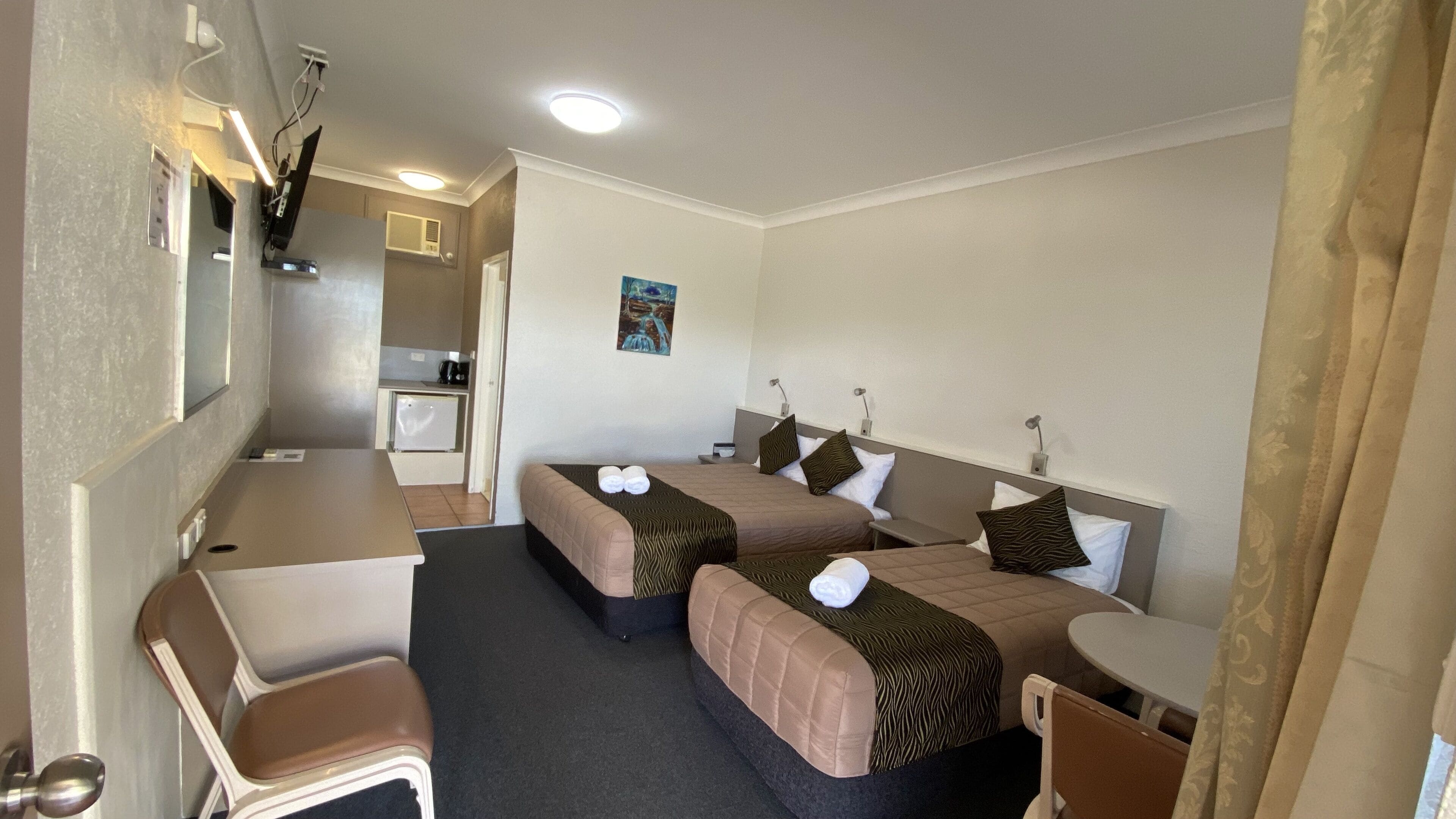 Una habitación de hotel compacta con dos camas, una kitchenette pequeña y un escritorio.