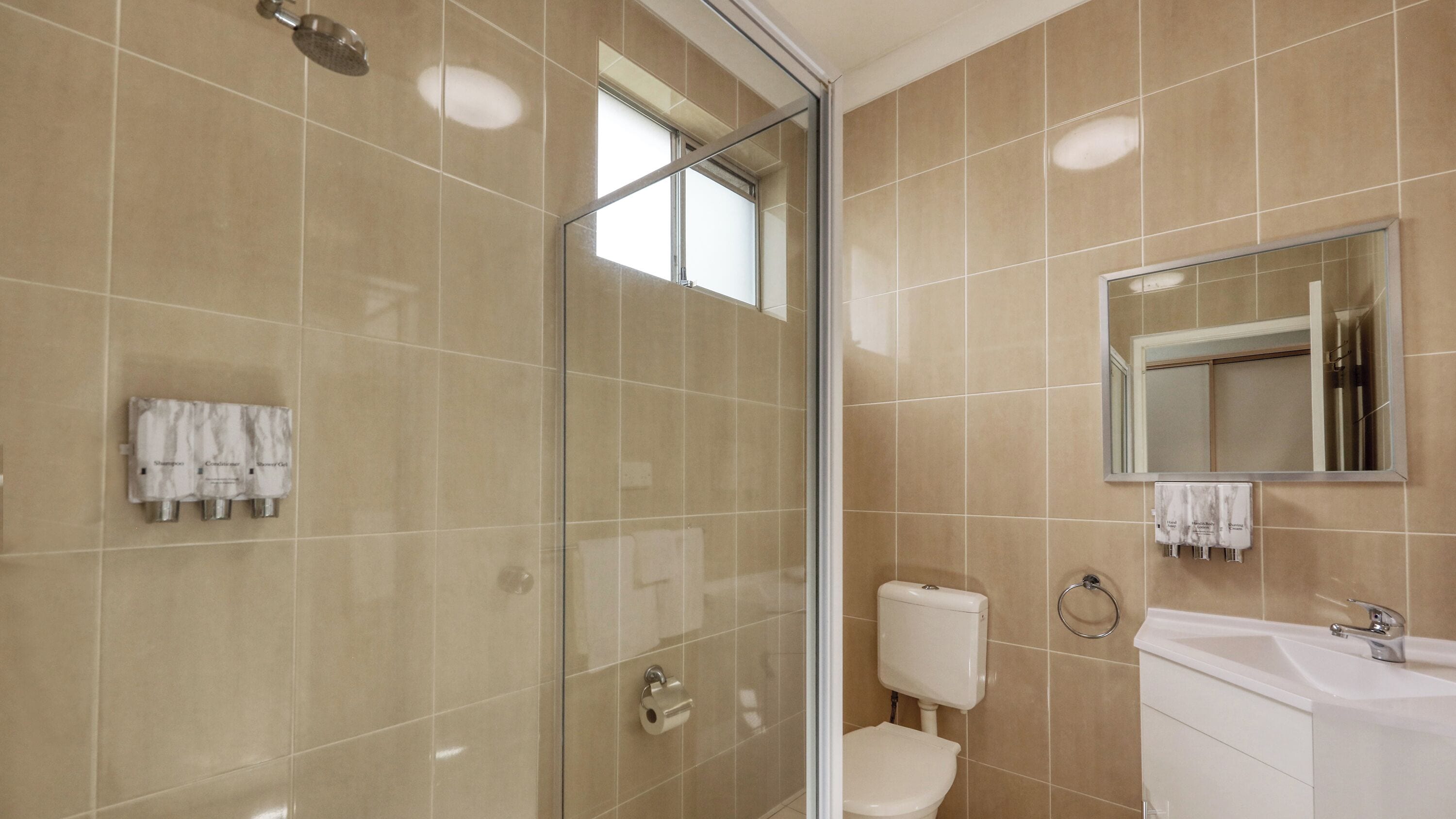 Ein modernes Badezimmer mit Duschkabine aus Glas, Toilette, Waschbecken und Spiegel.