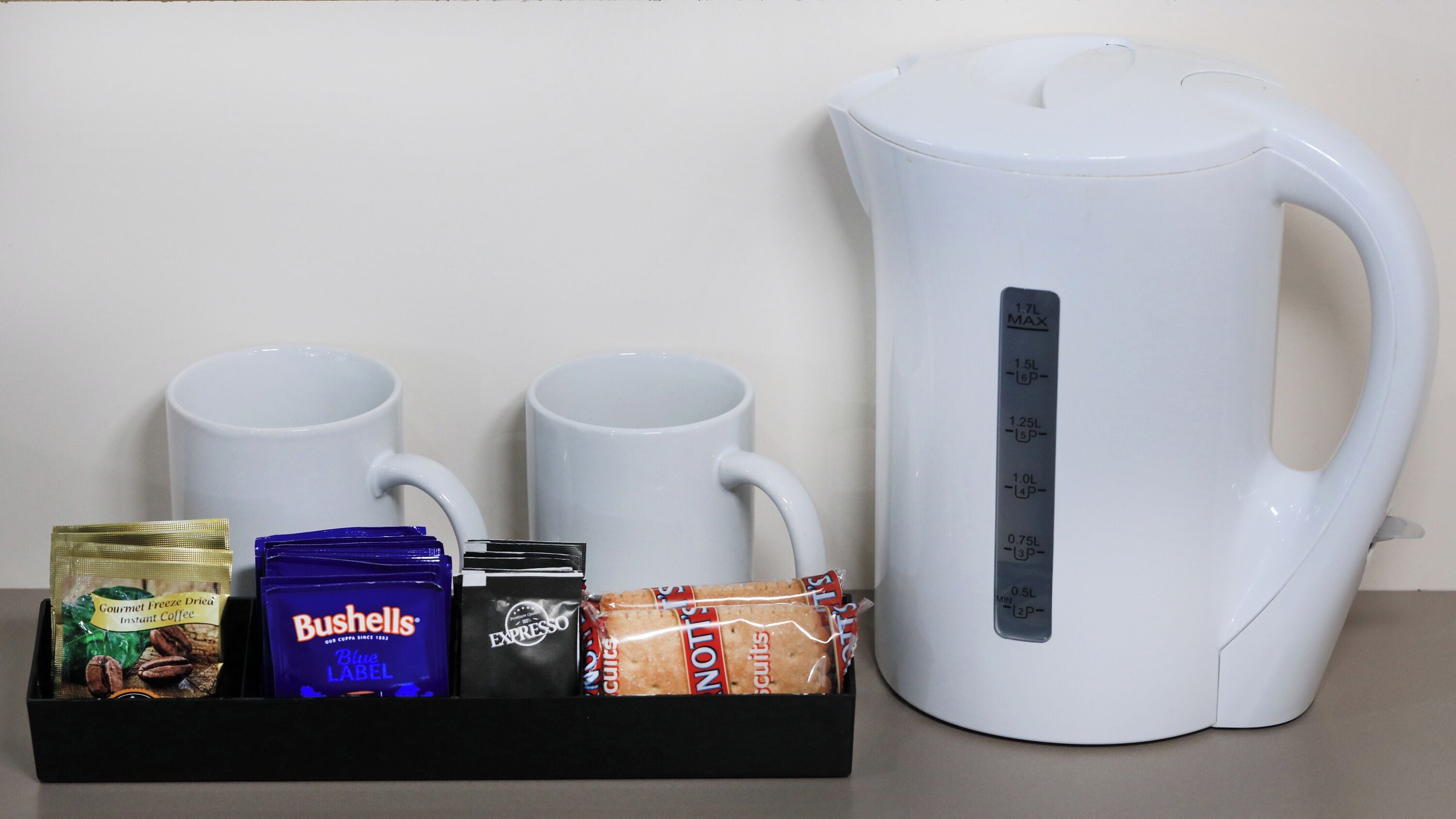 Una cafetera, dos tazas, sobres de café instantáneo y una caja de galletas.