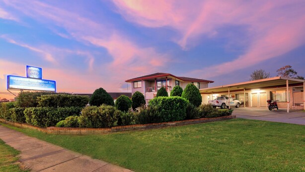 A motel with a landscaped front yard, a covered parking area, and a signboard advertising services.