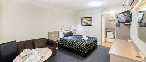 Habitación de hotel con cama, escritorio con computadora, kitchenette pequeña y zona de comedor con mesa para dos.