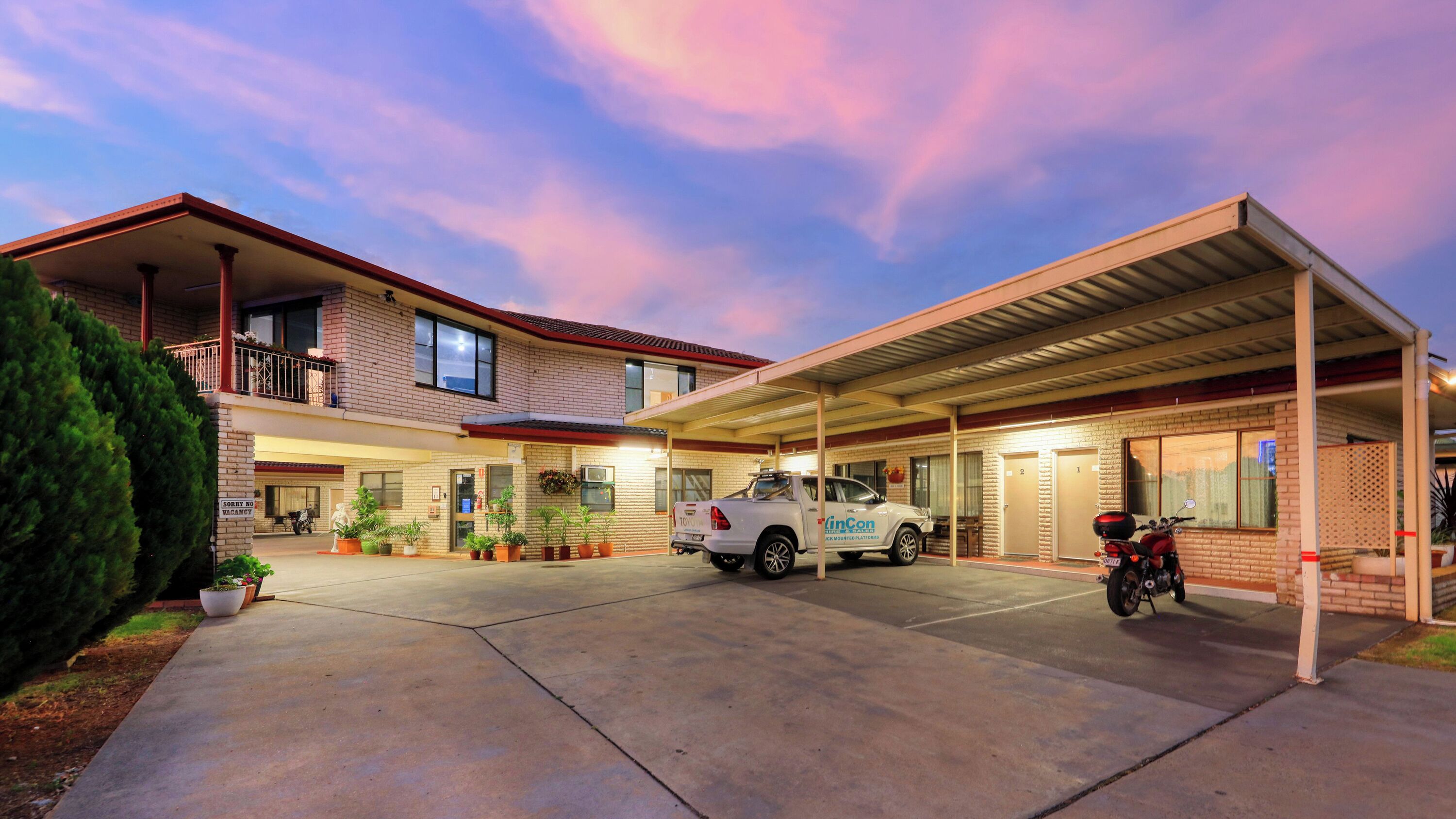 A motel with a covered parking area, a white truck, and a motorcycle parked outside.