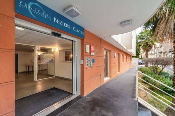 The entrance to the Zenith Hotel Residences Béziers Centre with a clear glass door, a reception desk inside, and a small outdoor seating area visible through the door. - Zenitude Hôtel Résidences Beziers Centre (Béziers)