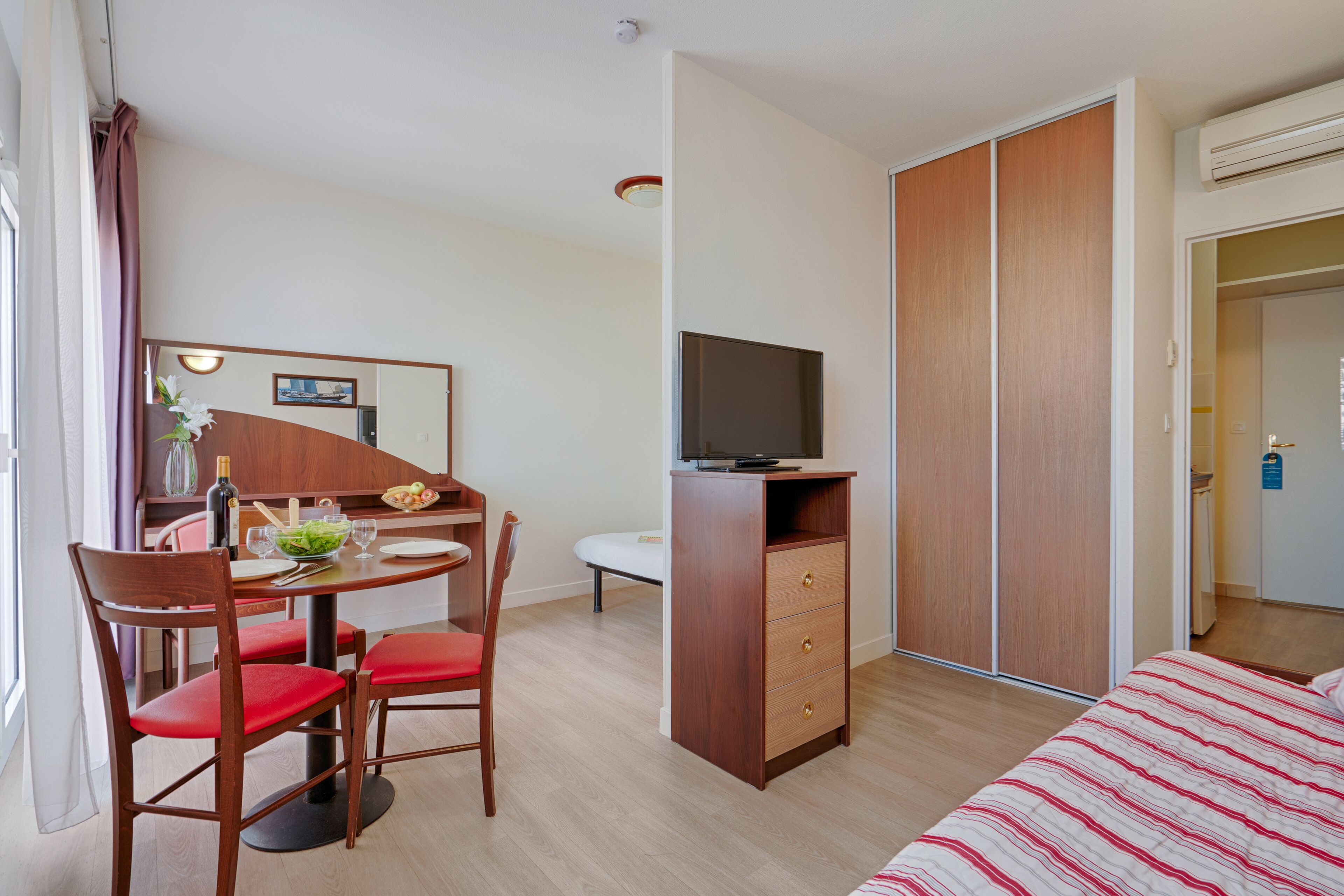 Een hotelkamer met een eethoek, televisie, kledingkast en bed.