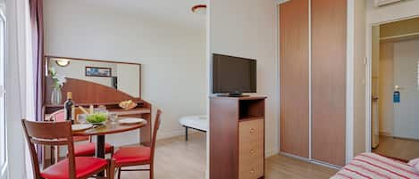 Een hotelkamer met een eethoek, televisie, kledingkast en bed.