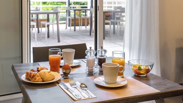 Una mesa de desayuno con croissants, un vaso de zumo de naranja y un bol de fruta.
