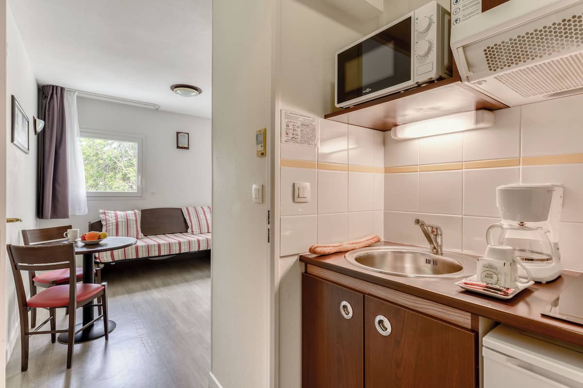 A compact kitchenette with a microwave, toaster, and coffee maker. There is a dining area with a table and chairs, and a window with curtains.