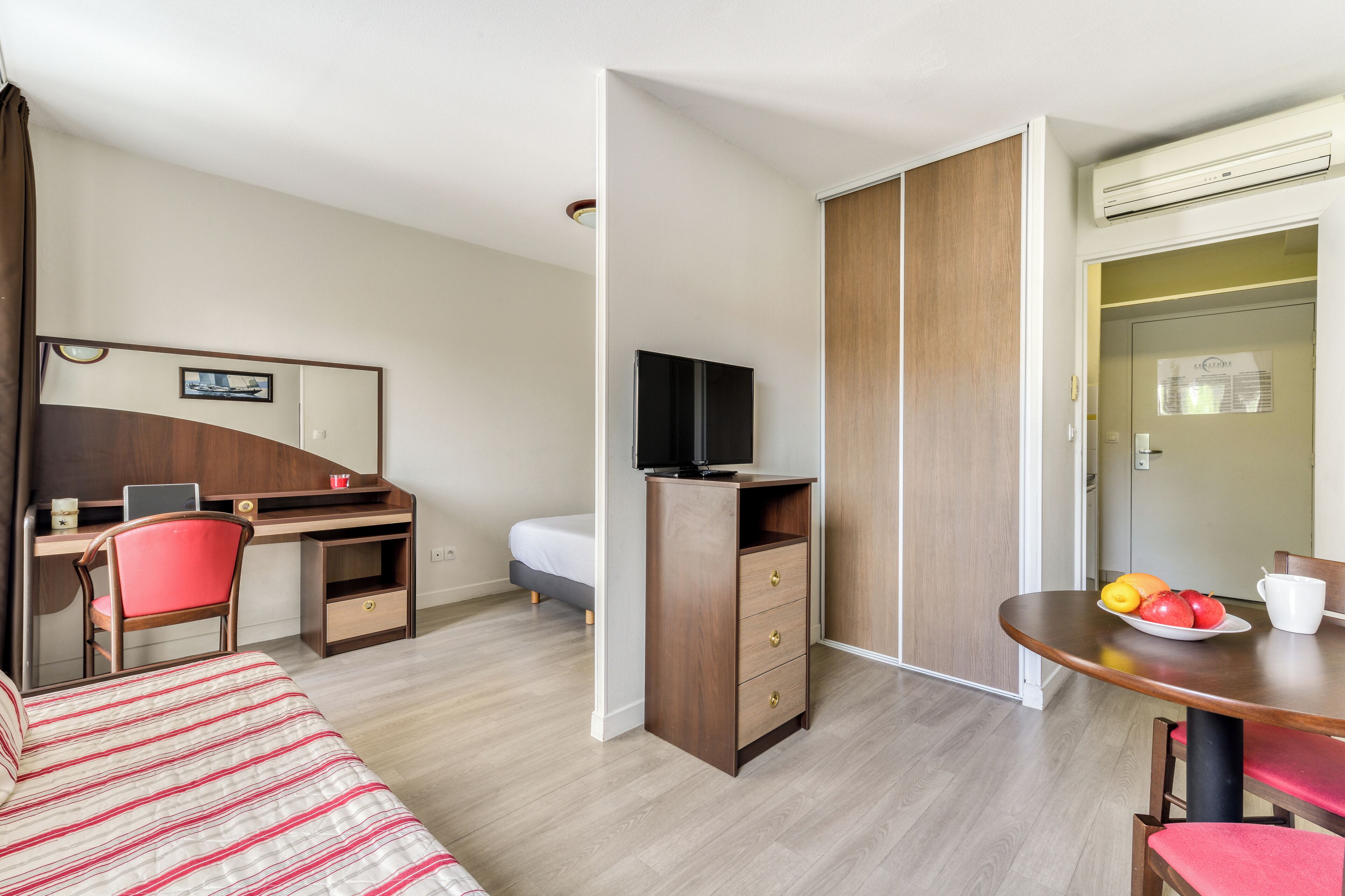 Camera d'albergo con un letto, una scrivania con sedia, una televisione, un armadio e un tavolo da pranzo con frutta.