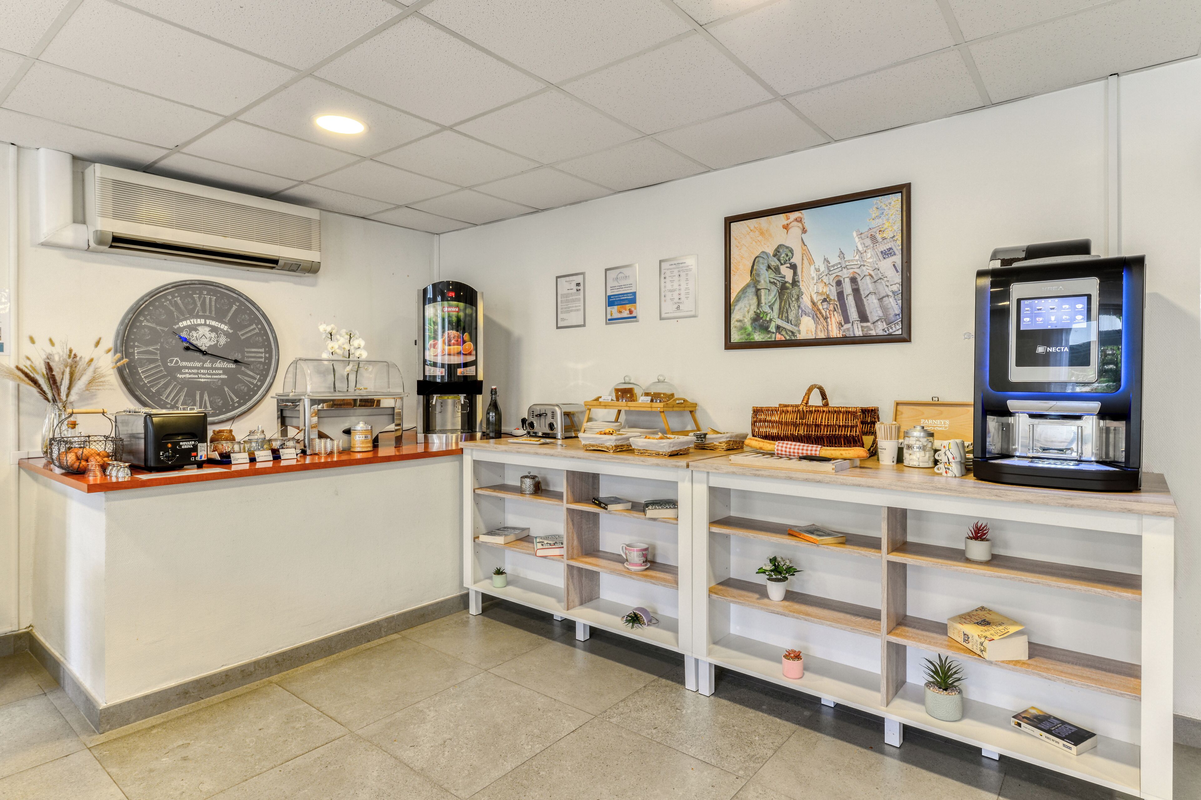 Un espace d’accueil comprenant une horloge, un climatiseur, des œuvres d’art encadrées et une machine à café.