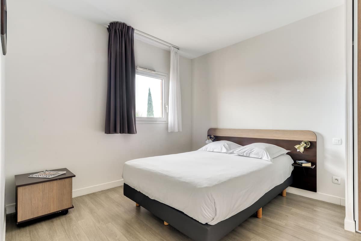 A modern bedroom with a bed, bedside table, and a window with curtains.