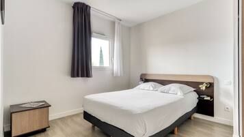 A modern bedroom with a bed, bedside table, and a window with curtains.