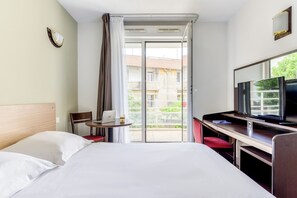 A hotel room with a bed, a desk with a laptop, a television, and a balcony with a view of buildings. - Zenitude Hôtel Résidences Beziers Centre (Béziers)