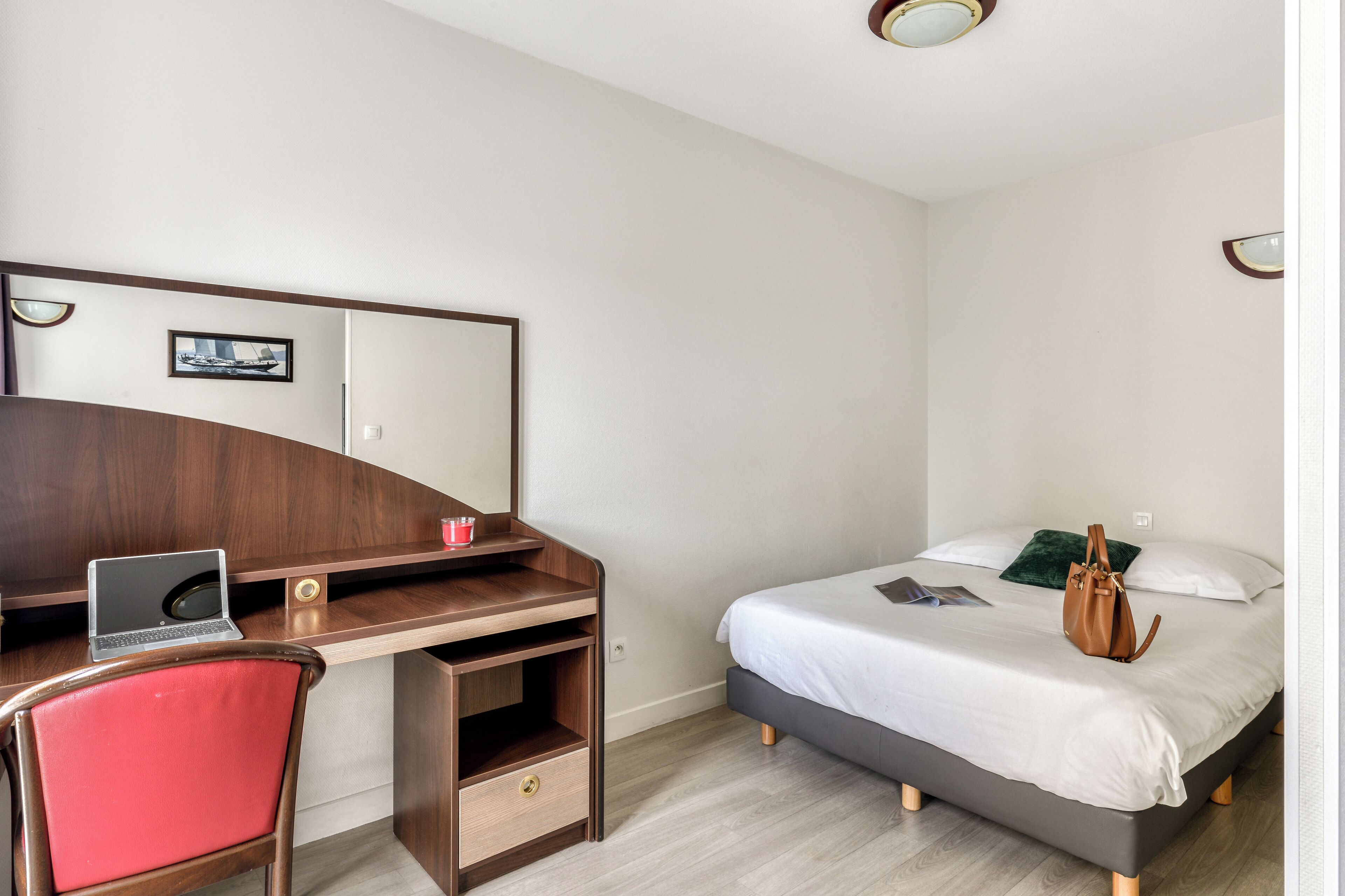 A bedroom with a bed, a desk with a laptop, a chair, and a bedside table.